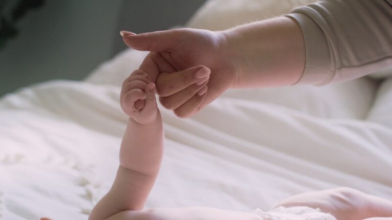 Infant holding parent’s finger while lying in bed