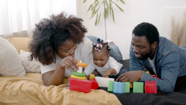 Two parents play with their baby on a bed, highlighting the importance of strong family planning support systems