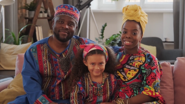 A smiling family sits together at home in colorful clothing, representing access to affordable family planning services