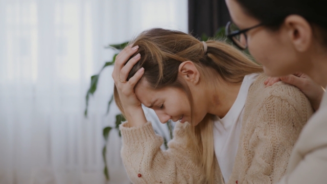 A woman breaks down in tears as another person offers support, reflecting the need for better postpartum and mental health care