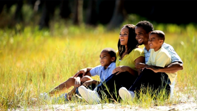 A happy family sits in a grassy field, showing the impact of family planning support