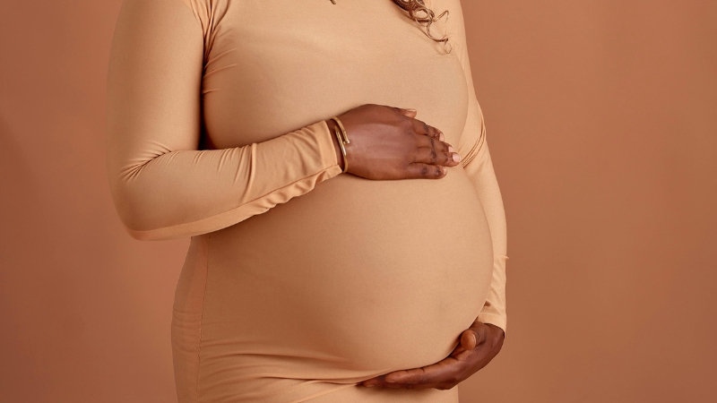 A pregnant woman holds her belly, reflecting the economic and social impact of falling below-replacement fertility