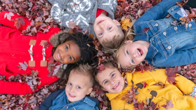 Children lying in autumn leaves represent future generations in the context of fertility and replacement rates